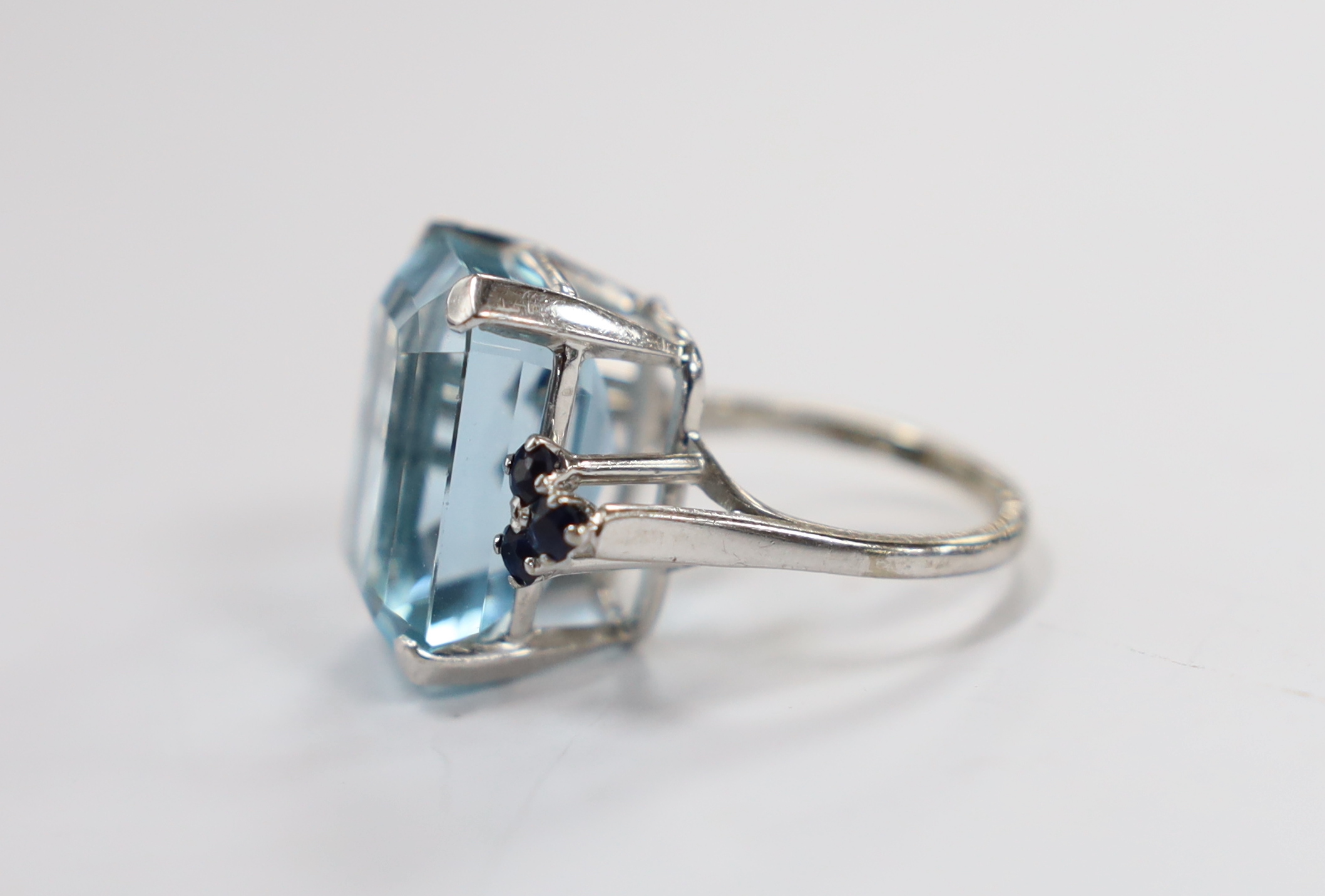 An 18ct white metal and single stone emerald cut aquamarines set dress ring, with six stone sapphire set shoulders, size L, gross weight 11.7 grams.